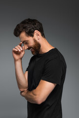 side view of cheerful man in black t-shirt smiling isolated on grey.