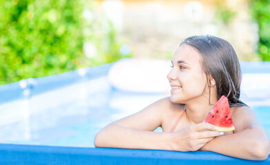 Smiling teen girl eats watermelon in the pool at sunny day. Empty space for text