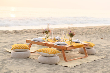 Small wooden decorated table placed on sandy seashore before romantic dinner