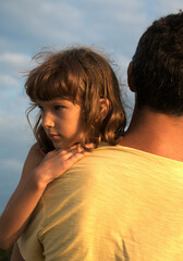 Emotions in parent-child relationships. Offended sad female child in the arms of dad looks to the side