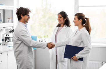 science, work and people concept - international group of happy scientists shaking hands in...