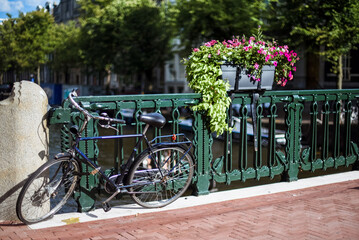 Fototapeta na wymiar Bicicleta aparcada en un puente de Ámsterdam adornado con flores en un soleado día de verano