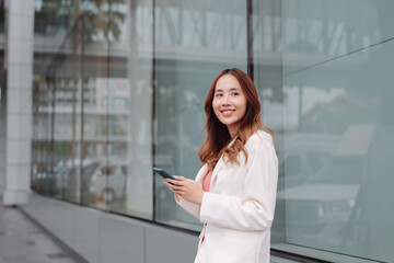 Fototapeta na wymiar Beautiful asian female businesswoman use smartphone, Walk enjoy smiling while doing commuting in the modern city near office building outside.