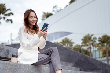 Beautiful asian female businesswoman use smartphone, Enjoy smiling while doing commuting in the modern city near office building outside..