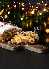 Stollen on the cut board with Christmas decoration and light. German fruit cake with nuts, spices, fruit and marzipan coated with powdered icing sugar