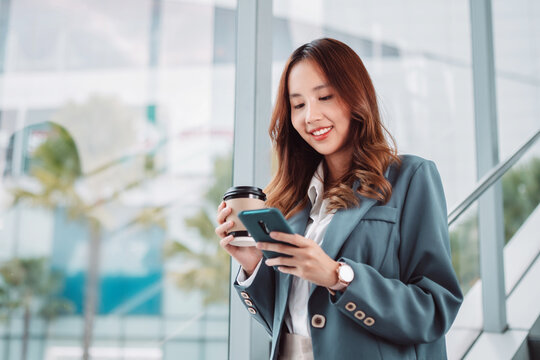 Beautiful asian female businesswoman use smartphone hold paper cup of hot drink, Walk enjoy smiling while doing commuting in the modern city at office