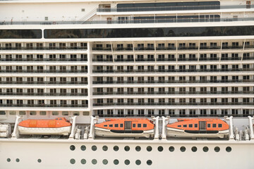 Close-up side view of large white passenger cruise line ship with many round cabin windows, balcony...