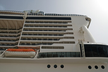 Close-up side view of large white passenger cruise line ship with many round cabin windows, balcony...