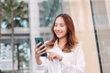 Beautiful asian female businesswoman use smartphone, Walk enjoy smiling while doing commuting in the modern city near office building outside.