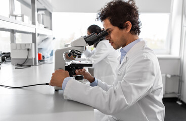 science research, work and people concept - male scientist with microscope working in laboratory