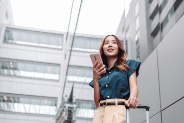 Beautiful asian female businesswoman use smartphone, Walk enjoy smiling while doing commuting in the modern city near office building outside