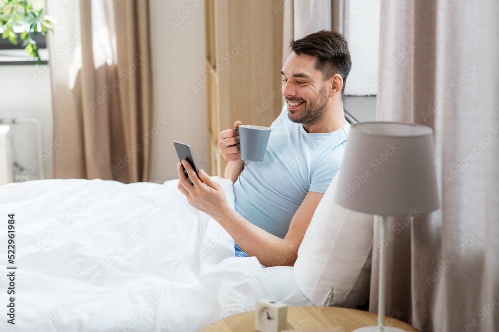 Canvas Prints people, bedtime and rest concept - happy smiling man with smartphone drinking coffee in bed at home