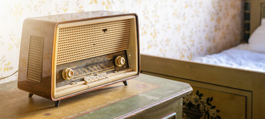 Old retro vintage radio on a aged wooden table illuminated by the sun - Aged bedroom or hotel room