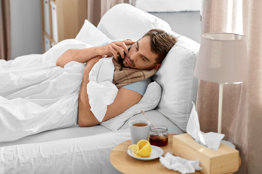 health, illness and people concept - sick man calling on smartphone in bed at home