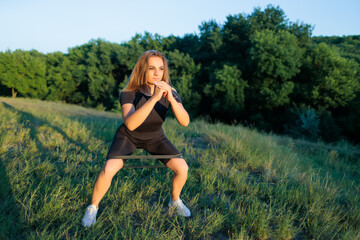 Fitness blonde doing squats with rubber bands on her legs