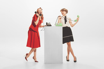 Portrait of two stylish woman in retro clothes talking on vintage phone isolated over white studio...
