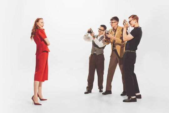 Group of young men in stylish suits taking photo of beautiful woman in red dress isolated over white studio background