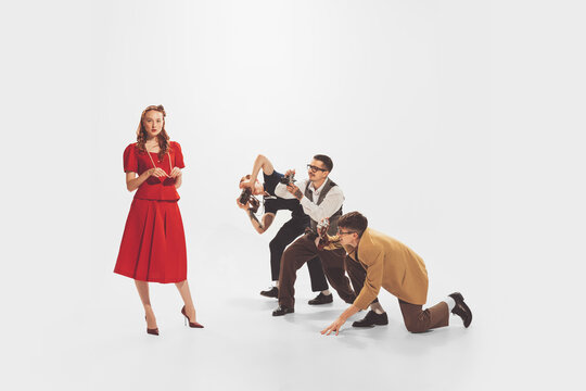 Group of young men in stylish suits taking photo of beautiful woman in red dress isolated over white studio background. Popularity