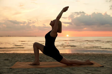 Fototapeta na wymiar fitness, sport, and healthy lifestyle concept - woman doing yoga low lunge on beach over sunset