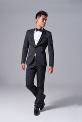 Handsome fashion model.
Full body elegant man wear formal black suit with bow tie on gray...