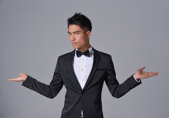 Handsome fashion model.
elegant man wear formal black suit with bow tie ,open hands on gray...