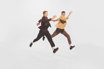 Fototapeta na wymiar Portrait of two stylish men, friends spending time together, posing in a jump isolated over white studio background