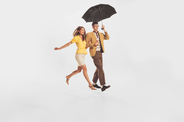 Portrait of young stylish couple, man and woman walking under umbrella isolated over white studio background