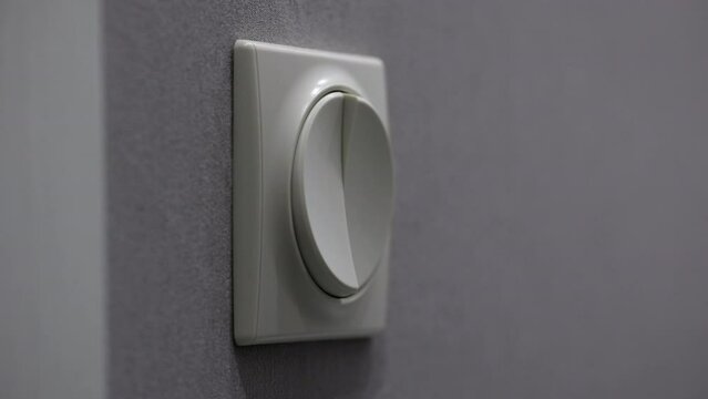 Beige Plastic Light Switch On A Purple Wall Is Turned Off By A Man's Hand. Close Up Indoor. Man Finger Pushing Light Switch Turn Off.