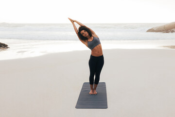Young woman practicing yoga at sunset. Fitness female doing side stretches on a beach.