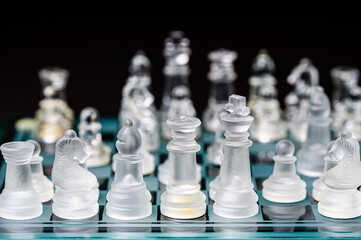 glass, transparent chess pieces on a checkerboard, selective focus, close-up, isolated on black