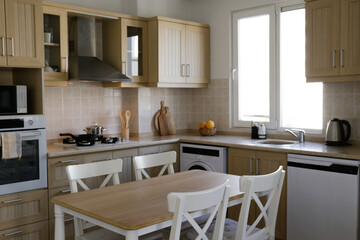 Stylish wooden kitchen with a window, built-in appliances and small beige tile. Close up, copy...