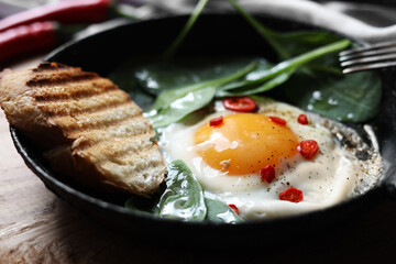 Delicious fried egg with spinach and chilli served on wooden table, closeup
