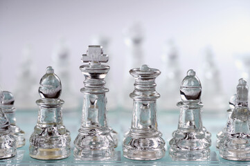 glass, transparent chess pieces on a checkerboard, selective focus, close-up, isolated on light