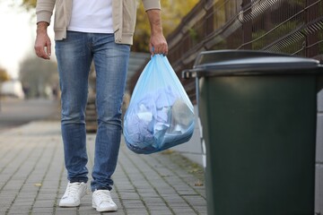 Man carrying garbage bag to recycling bin outdoors, closeup