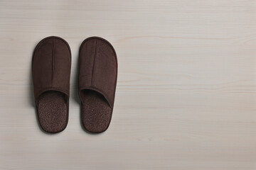 Pair of brown slippers on white wooden floor, top view. Space for text