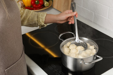 Woman cooking dumplings in saucepan with boiling water on cooktop, closeup