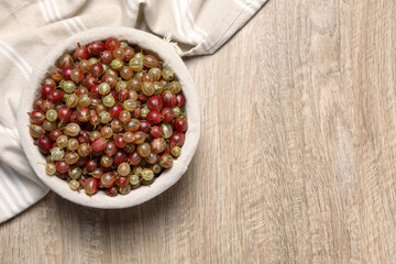 Fresh ripe gooseberries in bowl on wooden table, top view. Space for text