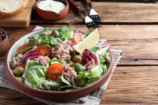 Plate of delicious salad with canned tuna and vegetables served on wooden table, space for text