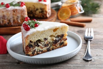 Fototapeta na wymiar Slice of traditional Christmas cake decorated with rosemary and cranberries on wooden table, closeup