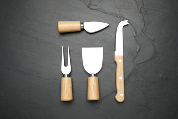 Cheese knives and fork on black stone table, flat lay