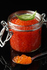 Delicious red caviar and basil leaf on black background