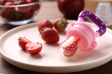 Plastic nibbler with fresh strawberries on plate, closeup. Baby feeder