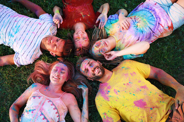 Happy friends covered with colorful powder dyes on green grass outdoors, above view. Holi festival...