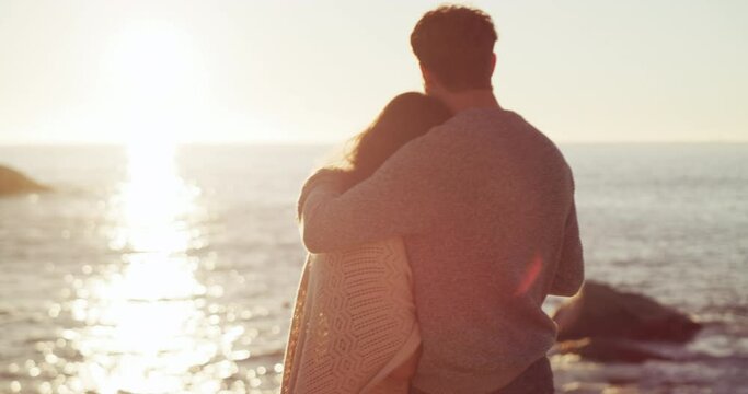 Husband and wife celebrating an anniversary, hugging and looking at the view of the sea on romantic holiday. Couple watching the sunset, drinking wine and bonding at the beach in nature from behind.