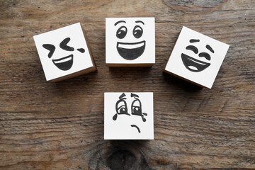 Cubes with sad and funny faces on wooden table, flat lay. Bullying concept