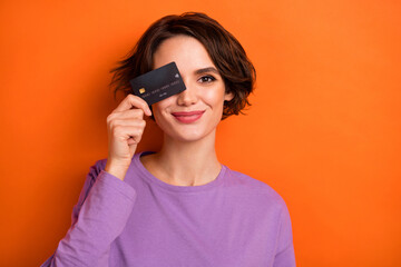 Photo of nice positive lady hold debit plastic card cover eye isolated on orange color background