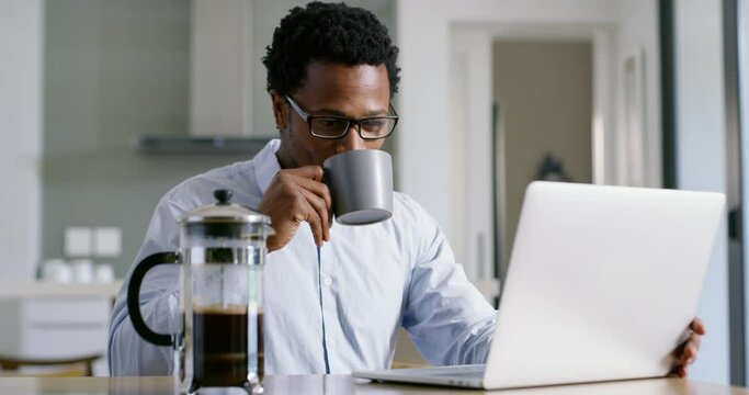Man on a laptop talking on a video call while looking happy, smiling and cheerful. Friendly young black business man on a webinar, drinking coffee and chatting to colleagues while in a modern kitchen