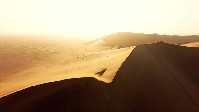 Hiking, adventure and drone view of a male hiker exploring sand dunes and rugged terrain in a hot, dry and arid desert wilderness. Man on a hike or journey on barren, sandy and rolling hills