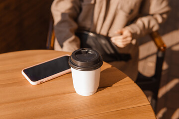 Fototapeta na wymiar Female hands with coffee and a mobile phone, close-up. Autumn walk