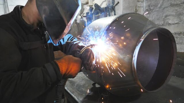 Welder doing joint between two steel details. Man welding parts of the metal detail together. Worker in protective mask welding metal construction at metalworking factory. Slow motion Close up